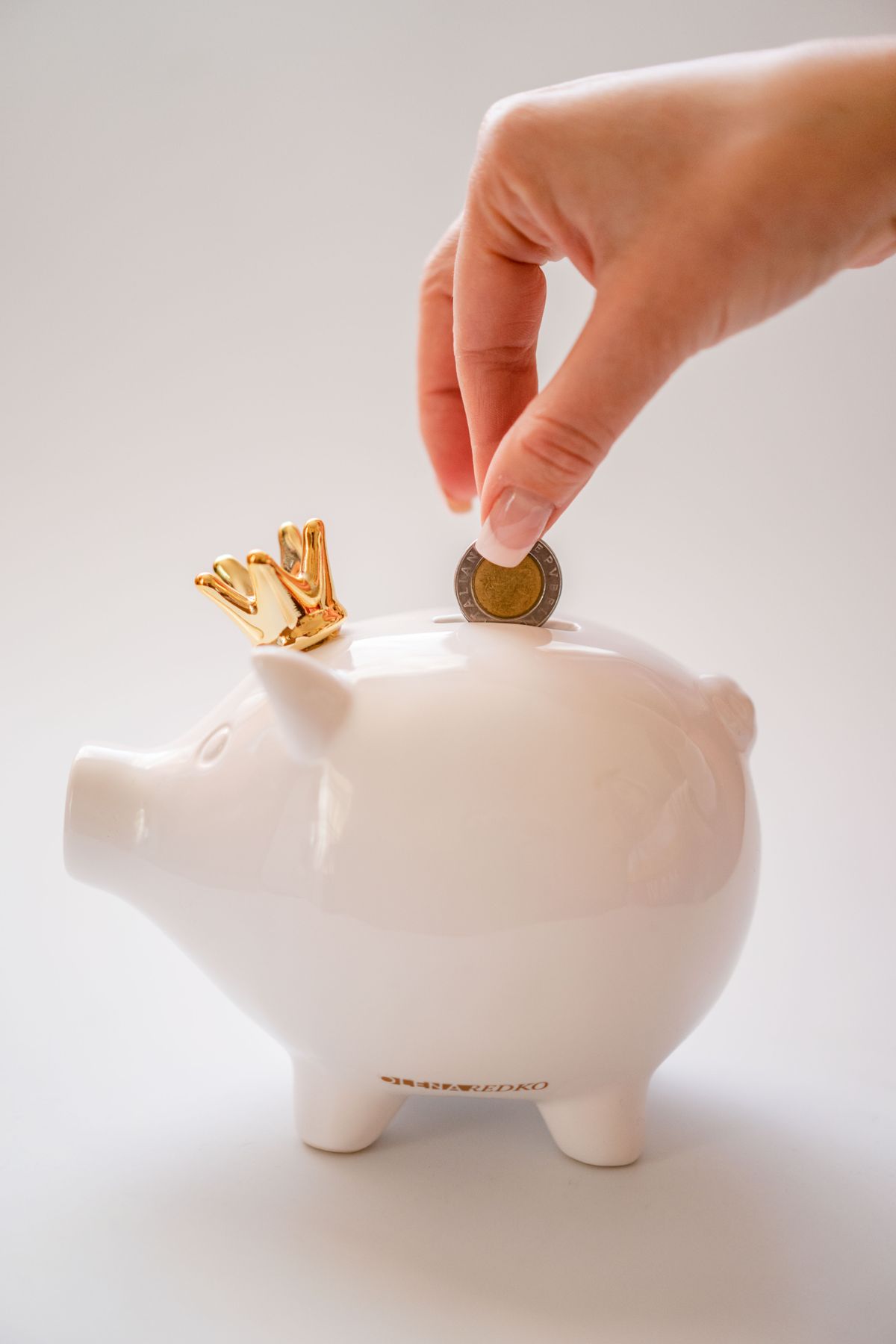A hand placing a coin into a piggy bank, representing a set spending limit