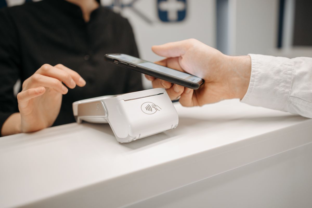 A person tapping a smartphone against a payment terminal to complete a contactless purchase