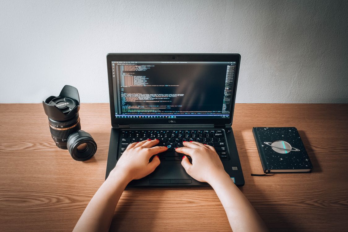 A woman working at a home desk with a camera and notebook nearby, representing a solo creator handling both content and administrative work.