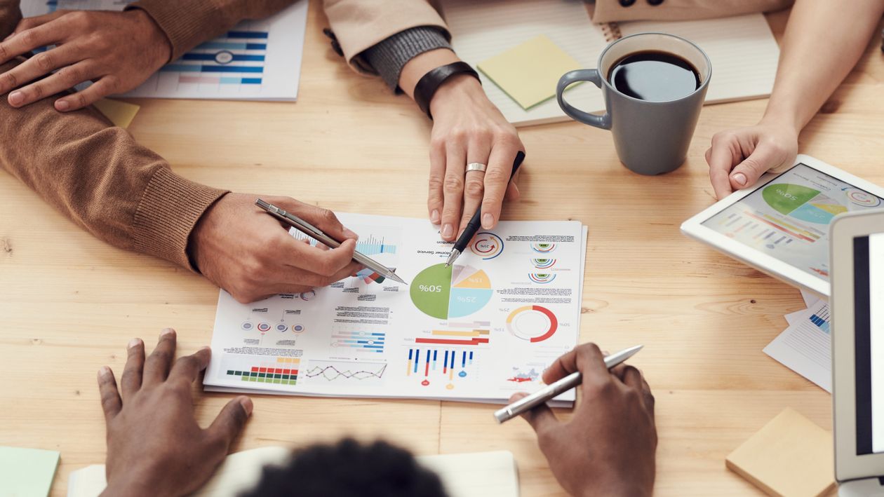 Colleagues gathered around a table reviewing charts and data together, illustrating a small team deciding what to hand off to an automated helper.
