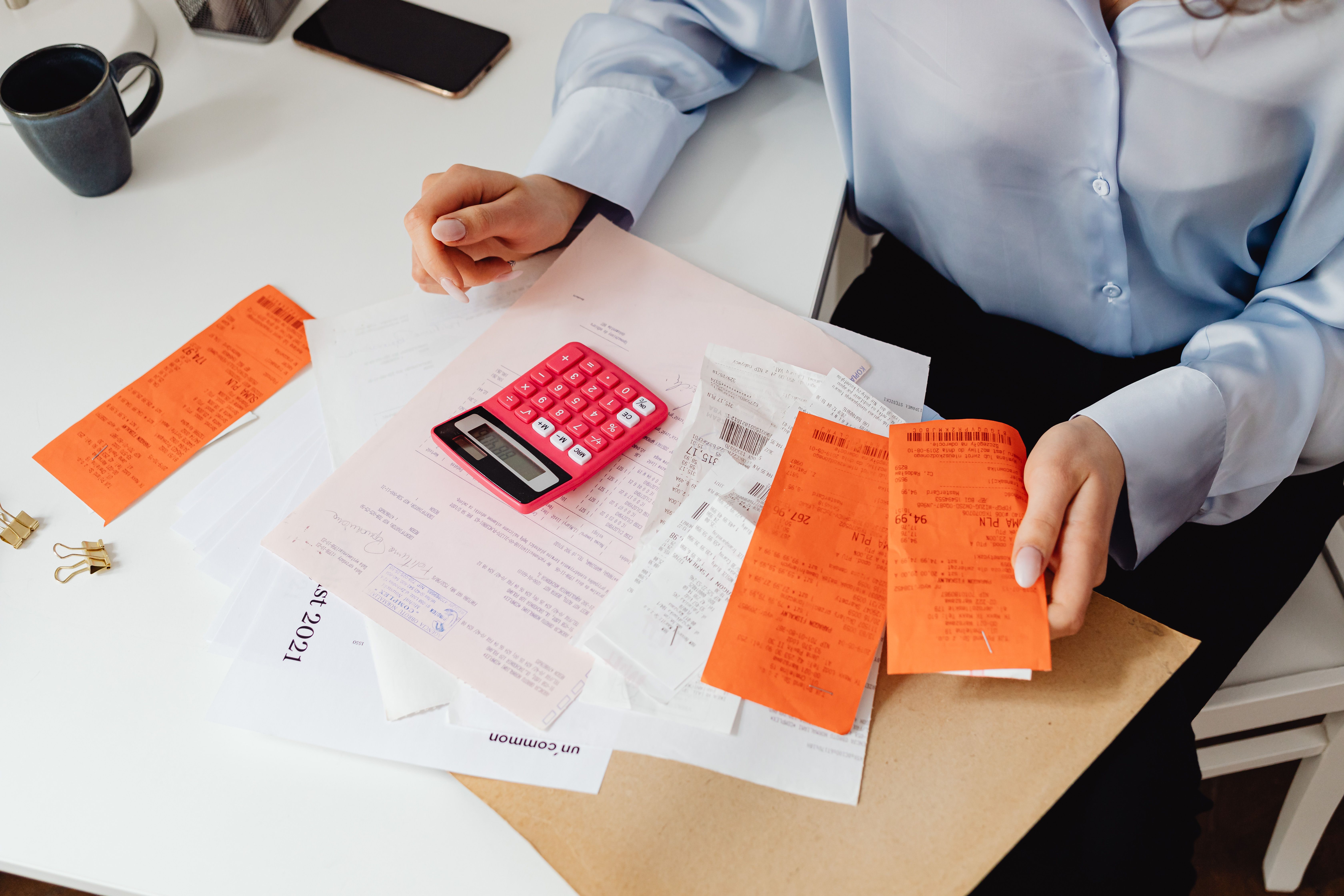 A person reviewing receipts and doing math on a calculator at a desk