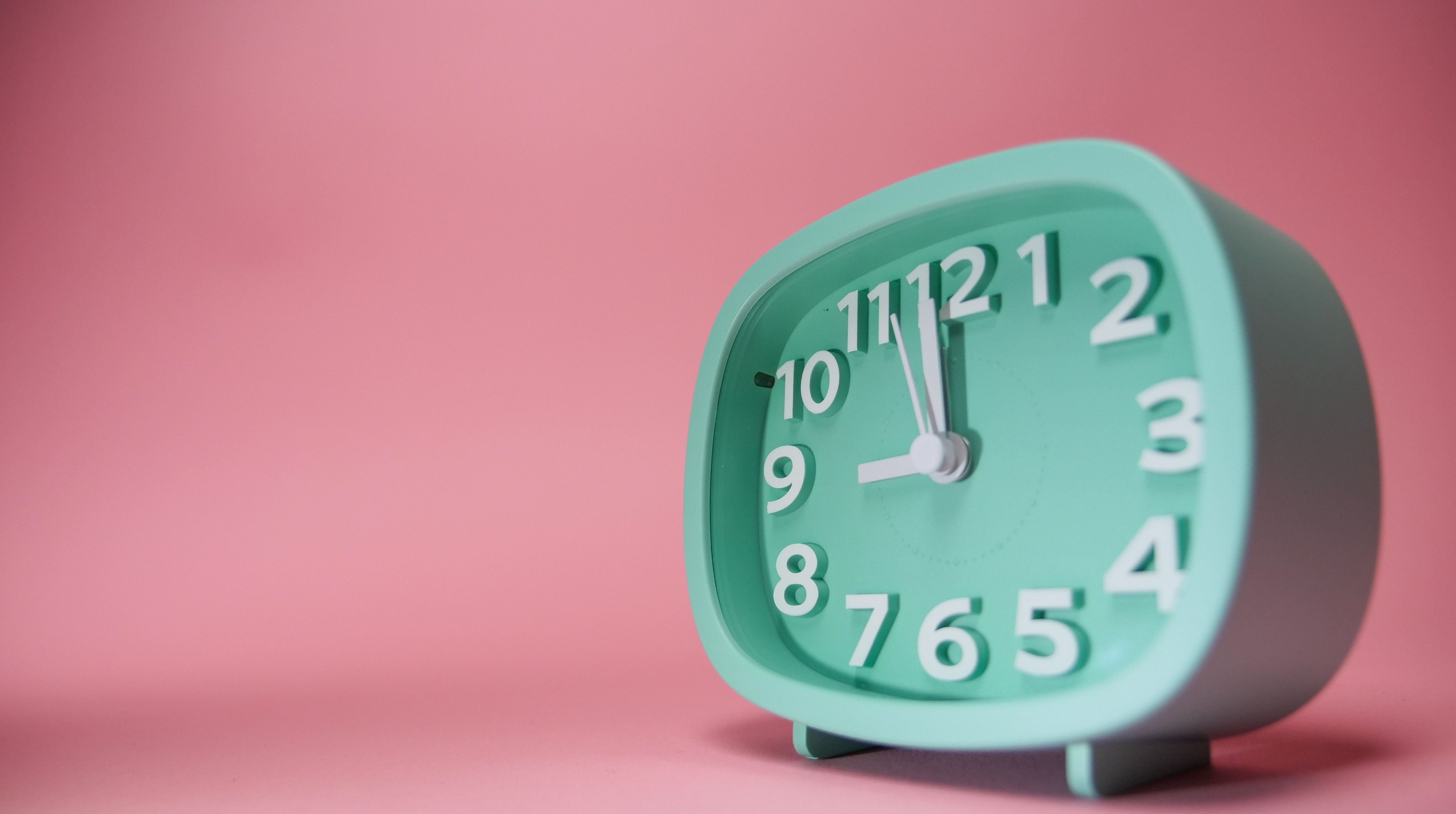 A mint green alarm clock against a pastel pink background