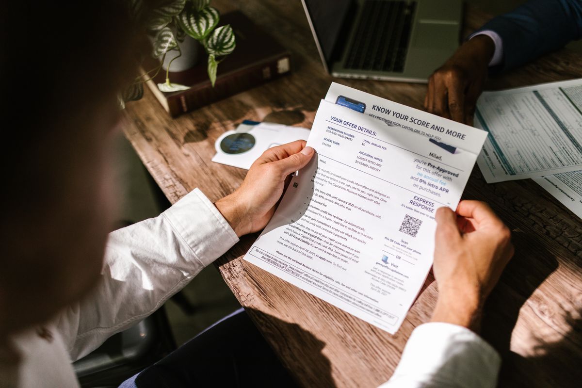 A person at a wooden desk reading through a printed document in natural light