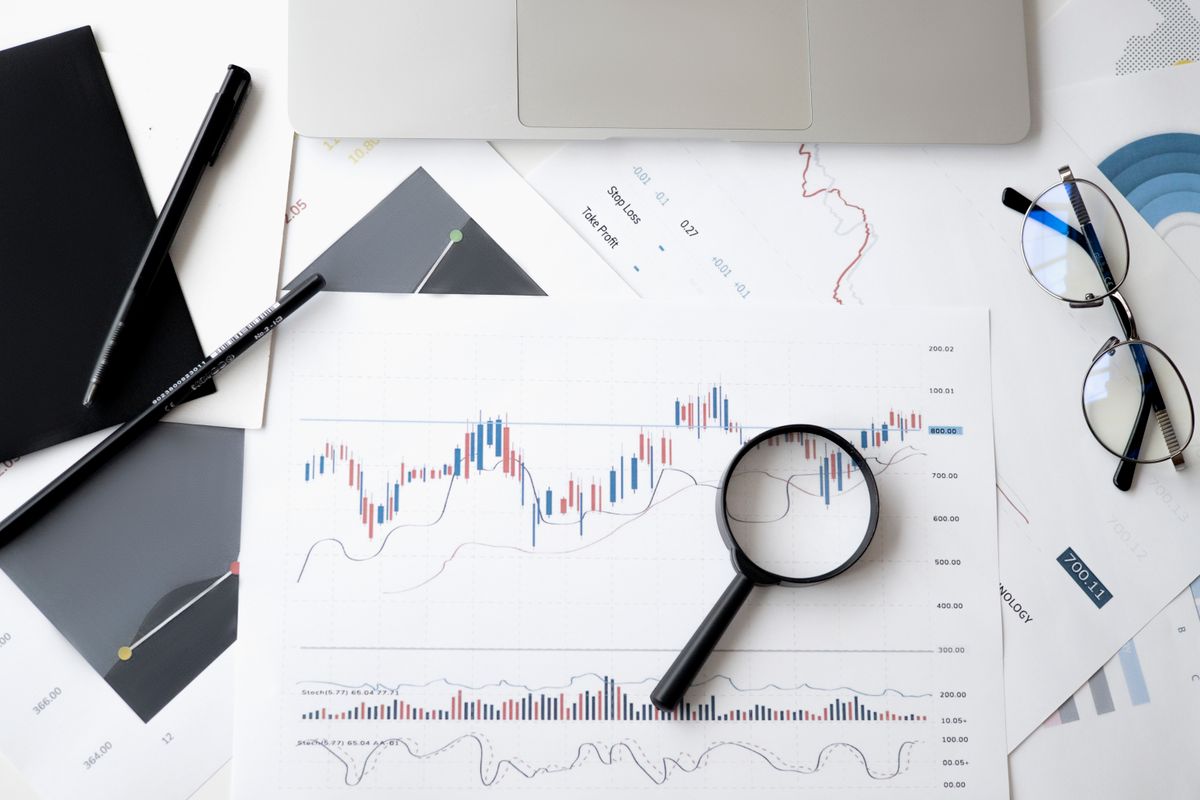 A magnifying glass laid over financial analysis documents, pens, and glasses on a desk, suggesting close reading of the fine print
