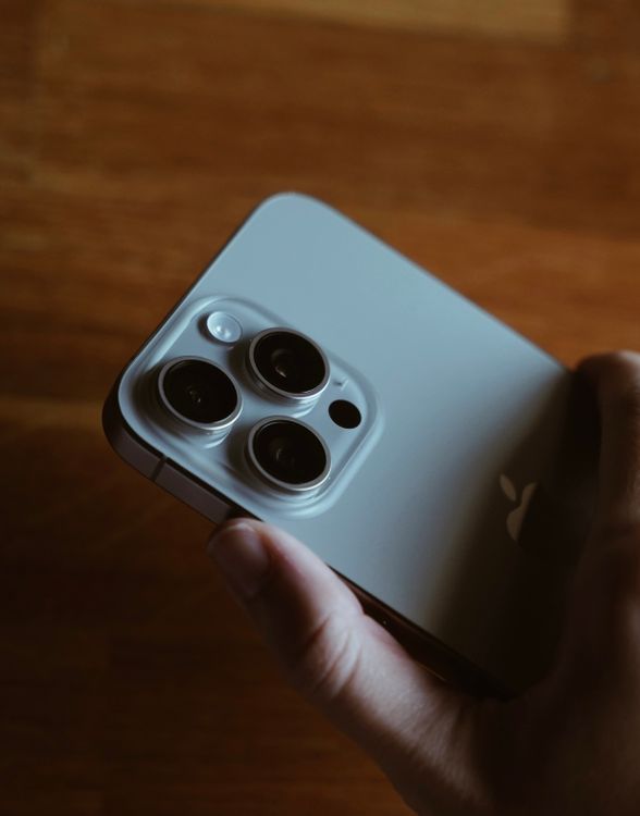 Close-up of a hand holding a modern iPhone with its triple-camera system visible, the kind of device Siri AI requires