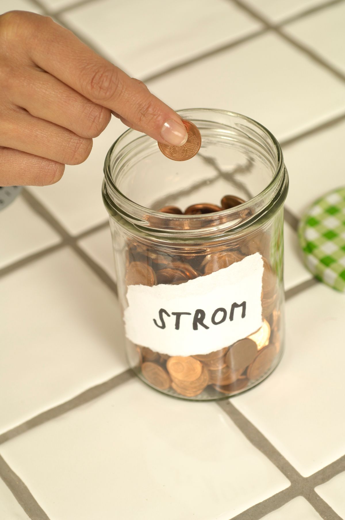 A hand dropping a coin into a glass savings jar